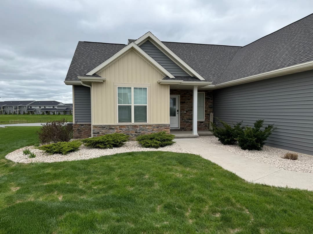 Modern house exterior with stone accents, well-maintained landscaping, and overcast sky.