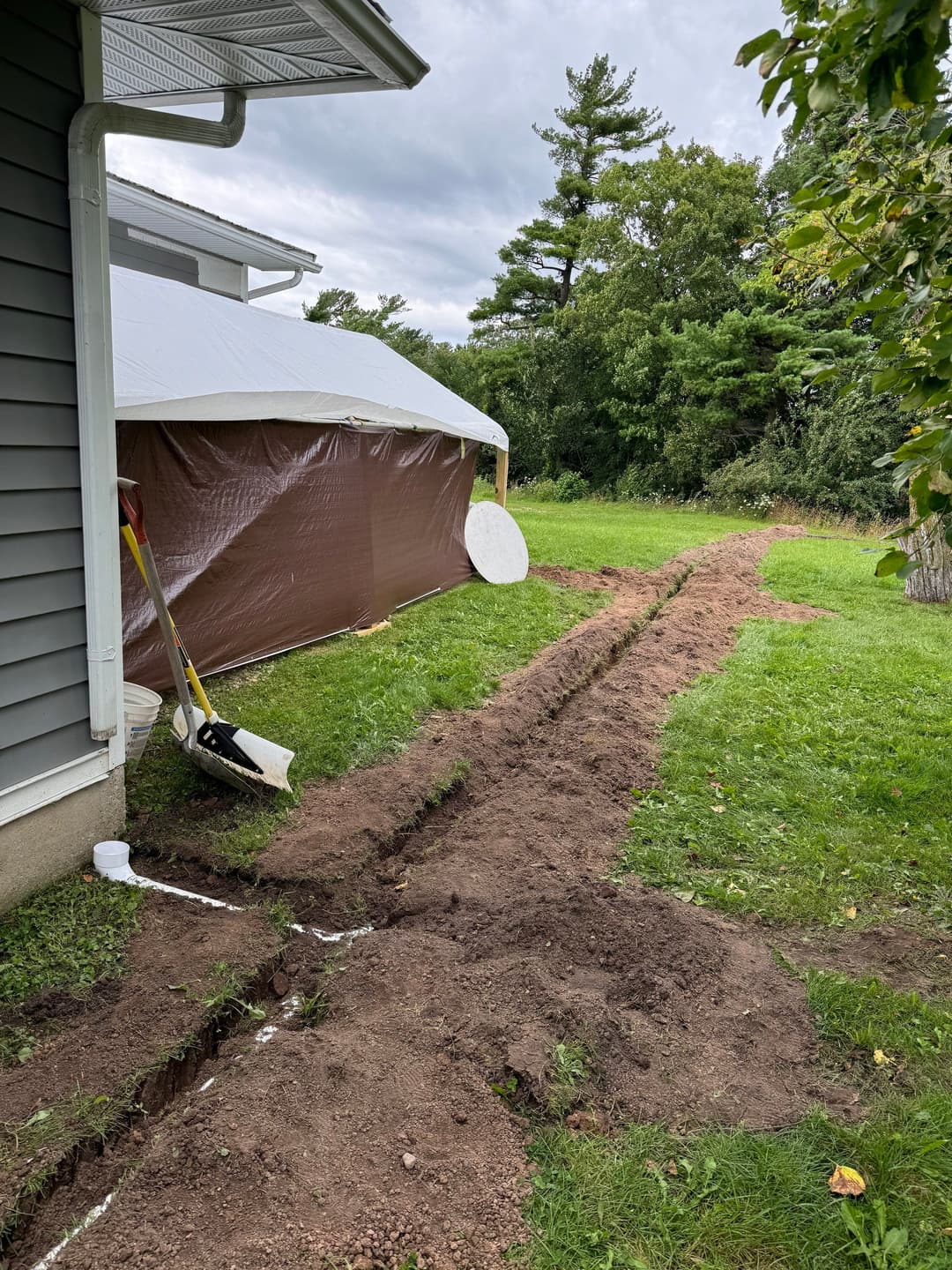 Excavated yard area next to house with a tent, spade, and drainage line installation.